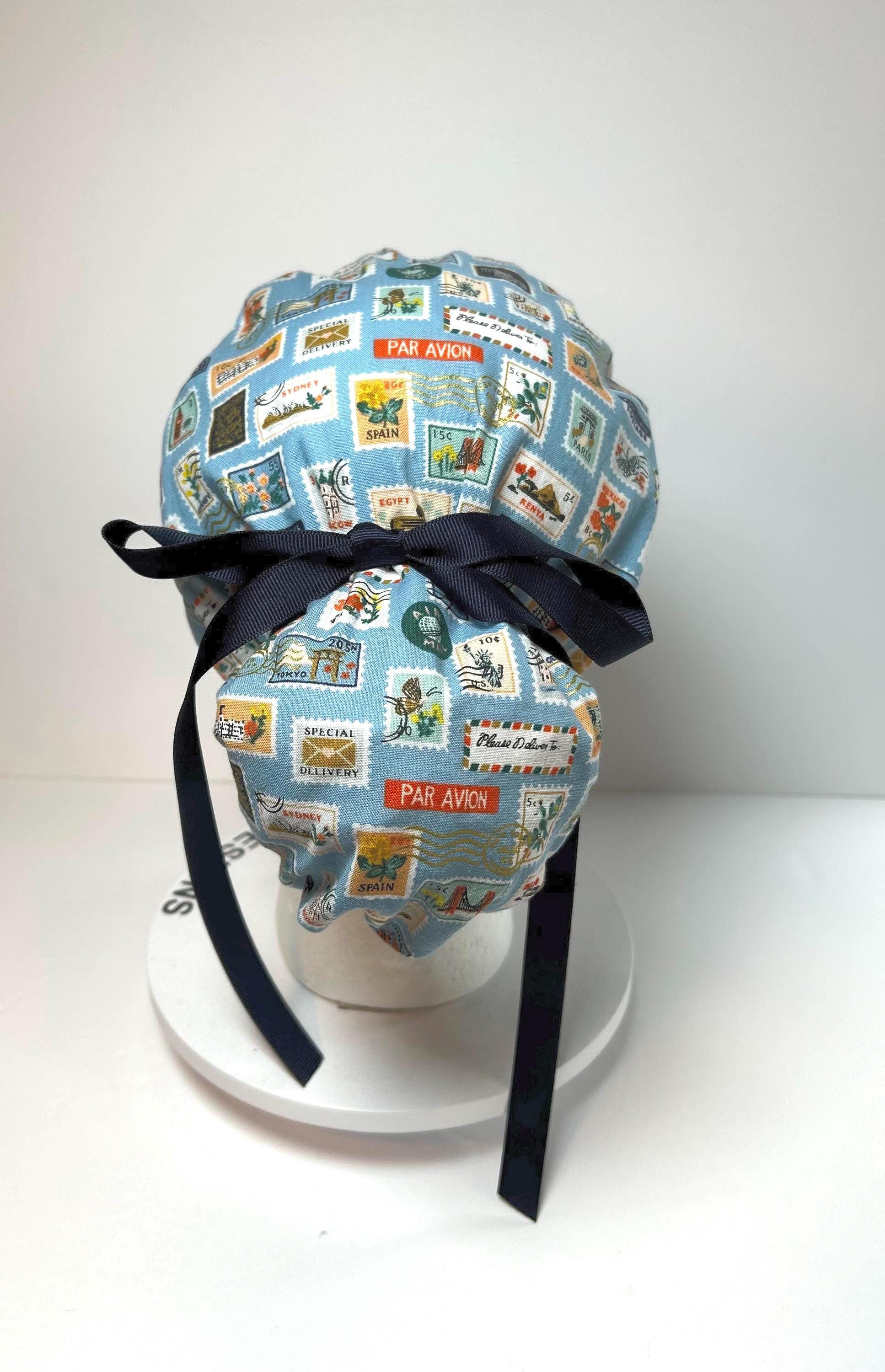 light blue ponytail scrub cap with travel stamp print and navy ribbon tied in a bow