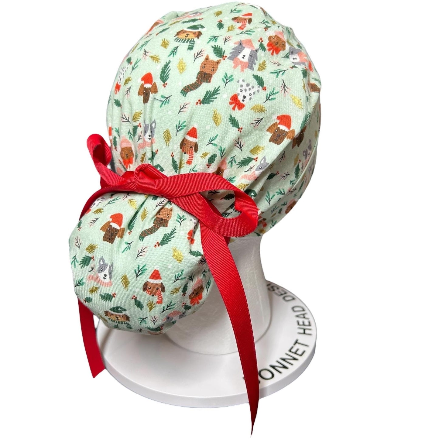 mint green cap with bun pocket sitting on a white stand. green fabric features small dogs wearing Christmas caps and the cap has a red ribbon