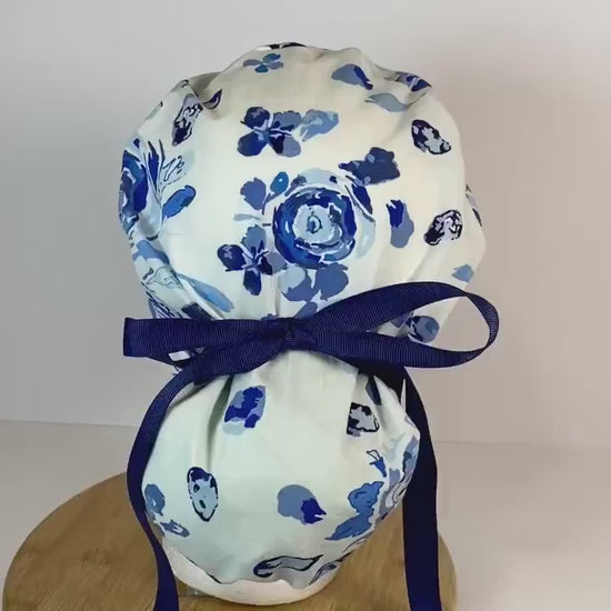 Shades of blue women’s floral scrub cap, blue, white, and navy floral ponytail scrub hat